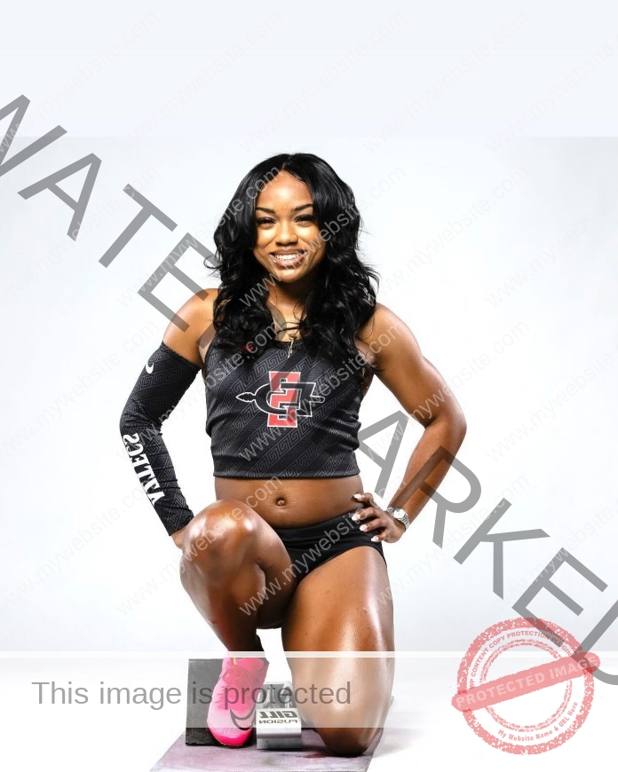 Sofia Iosifidou, track and field star from Greece, kneels on one knee, smiling in black gear with pink shoes and an SDSU logo top.