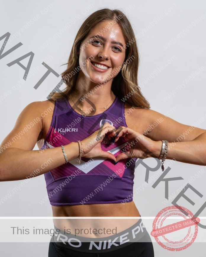 Molly Palmer, England track and field athlete, forms a heart with her hands in purple Kukri top and black Nike Pro shorts.