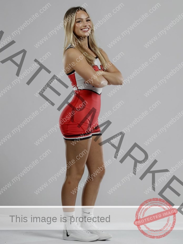 Nadia Thomas Nadia Thomas, in red and white athletic gear, stands sideways arms crossed, smiling; long blonde hair down; plain gray background.