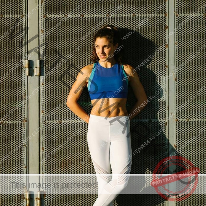 Nora Suarez Nora Suarez, a track and field athlete from Spain, stands by a metal fence in blue sports bra and white leggings, smiling.
