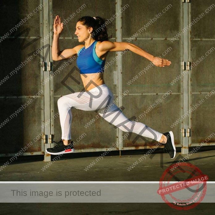 Nora Suarez Nora Suarez, a track and field athlete from Spain, leaps mid-air, knee bent, in blue sports bra and white leggings outside.
