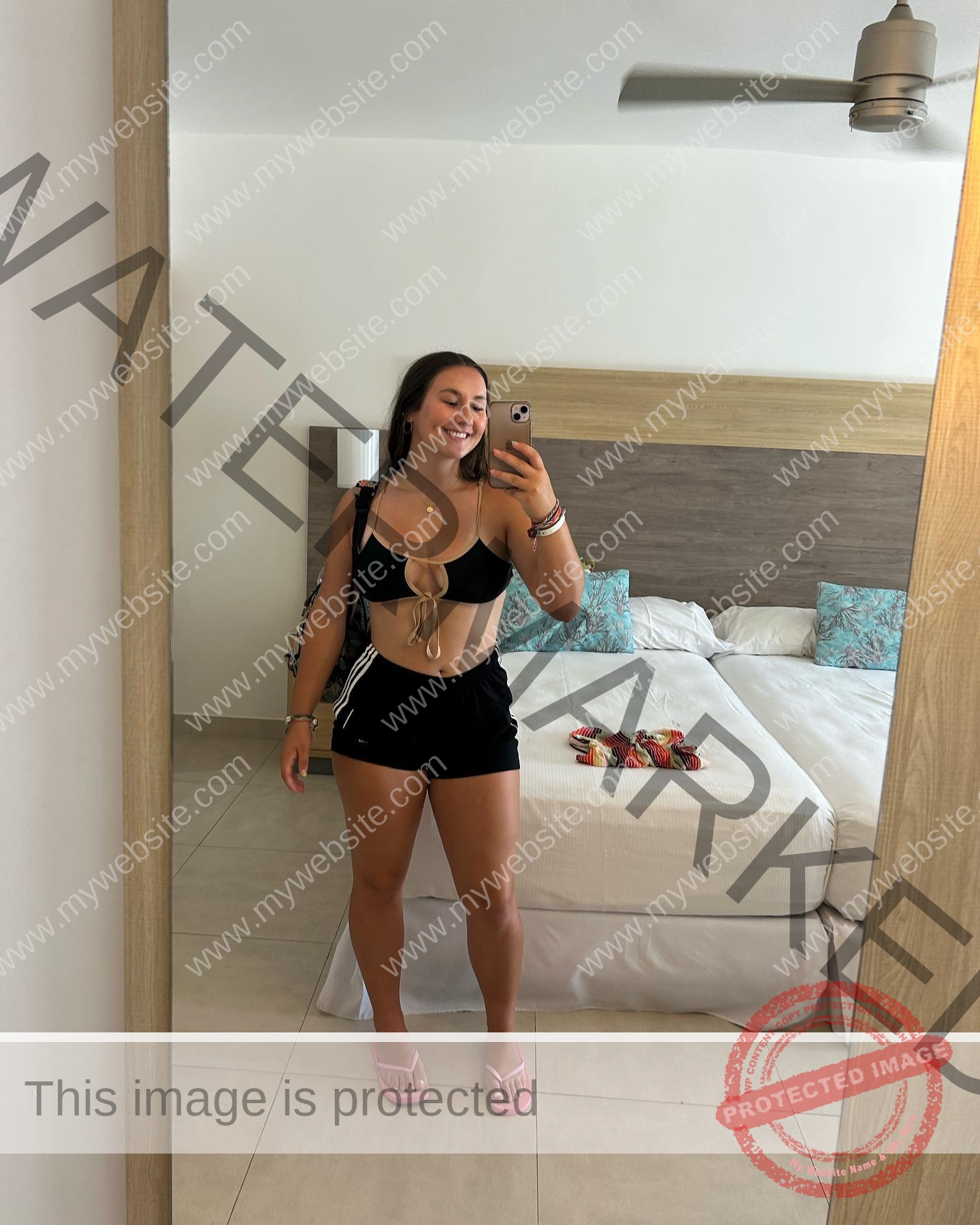 rosa-gergely-wake-forest-th-ro_gerg-08269 Rosa Gergely stands in front of a mirror taking a selfie in a bright bedroom, smiling in black crop top, shorts, and pink sandals.