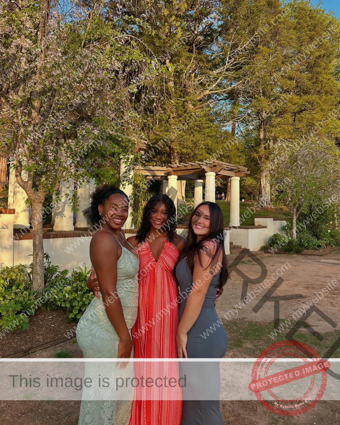 rosa-gergely-wake-forest-th-ro_gerg-08316 Rosa Gergely Three women in elegant dresses stand close together outside, smiling with trees and a white pergola after a track event.
