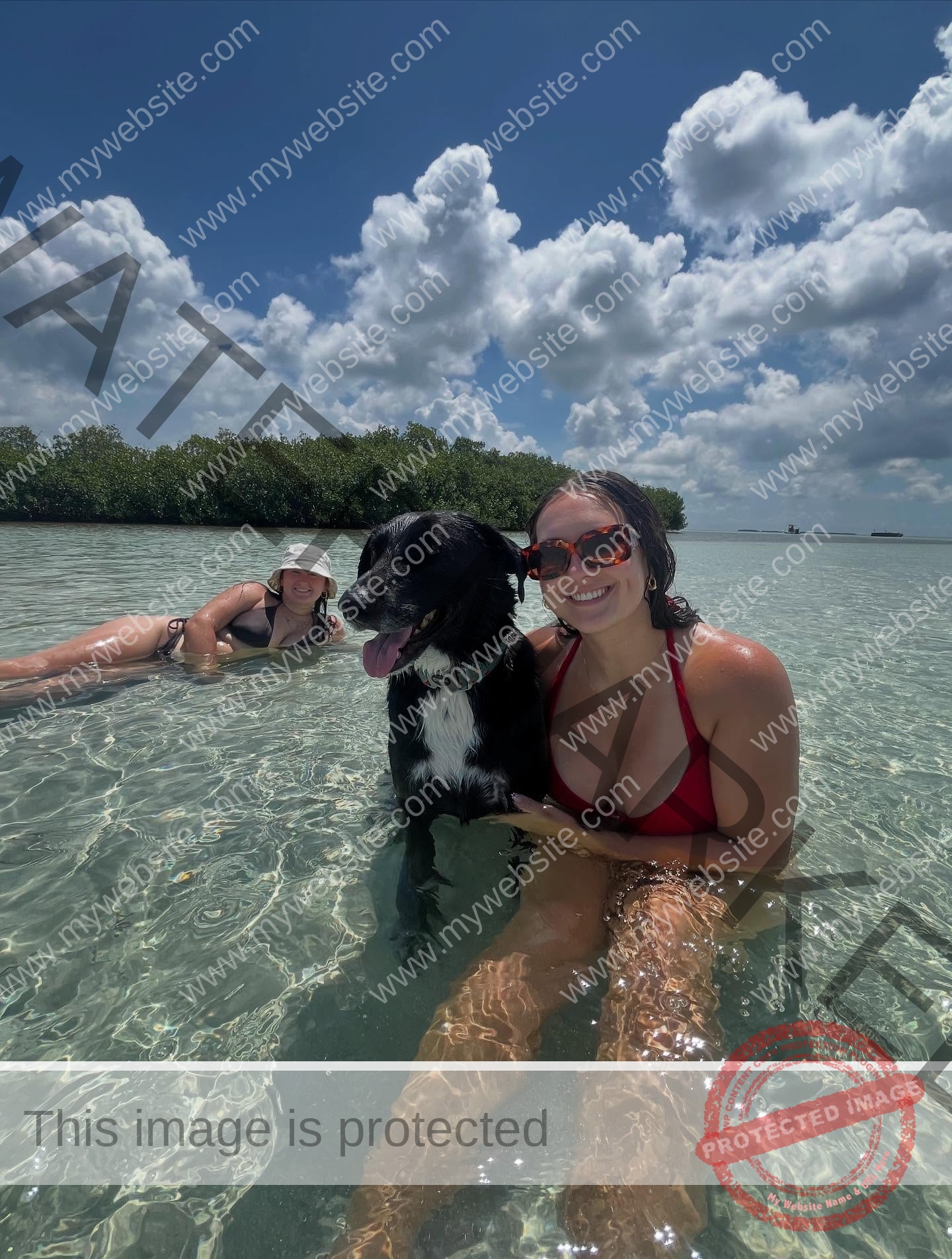 rosa-gergely-wake-forest-th-ro_gerg-08332 Rosa Gergely and another woman in swimwear, plus a black dog, enjoy shallow water under a sunny sky, smiling at the camera.
