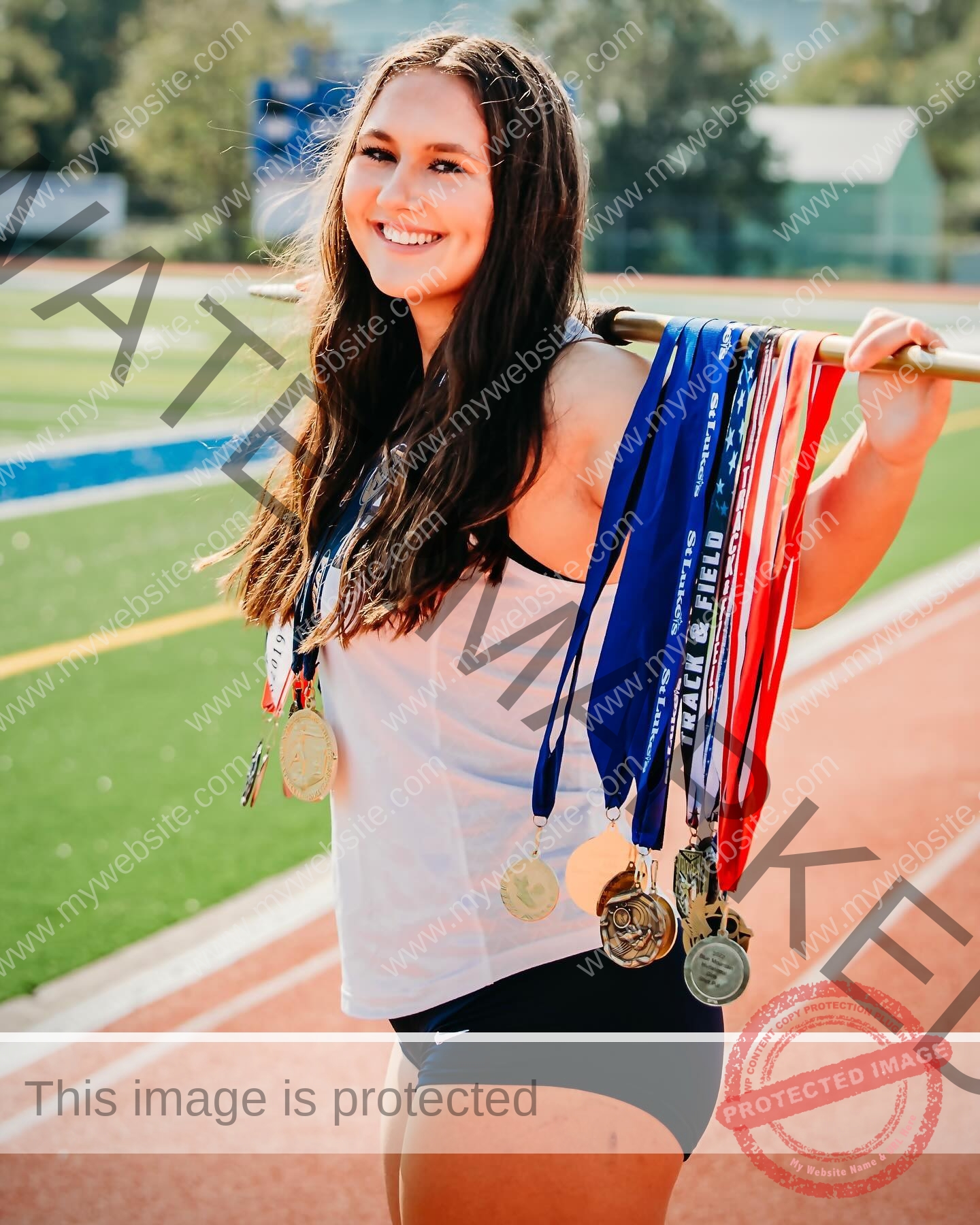 rosa-gergely-wake-forest-th-ro_gerg-1974 Rosa Gergely, javelin thrower from Wake Forest, stands on a running track smiling with medals on a pole, sports field behind her.