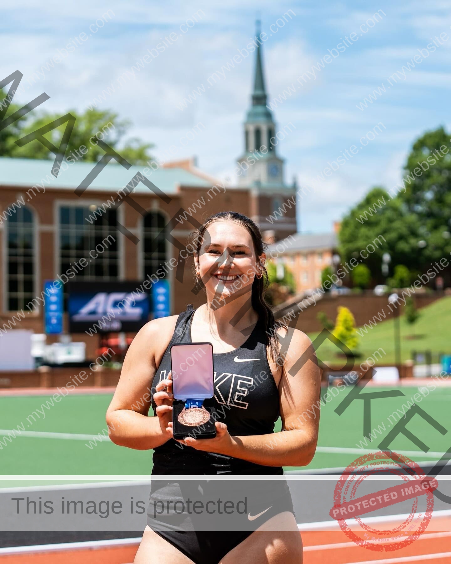 rosa-gergely-wake-forest-th-ro_gerg-2006 Rosa Gergely, javelin thrower from Wake Forest, stands on a track in black Nike attire, smiling and holding a medal in a red box.