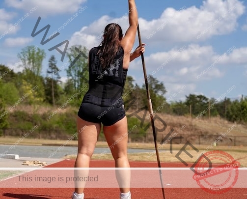 rosa-gergely-wake-forest-th-ro_gerg-2011 Rosa Gergely, javelin thrower from Wake Forest, stands on a red track holding a javelin upright, facing away, greenery behind.