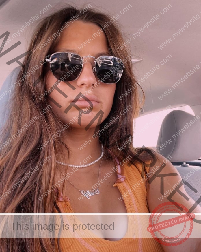 Sally Ann Ouzts, swimmer from Georgia Southern, with long brown hair and sunglasses in an orange top, sits in a sunlit car.