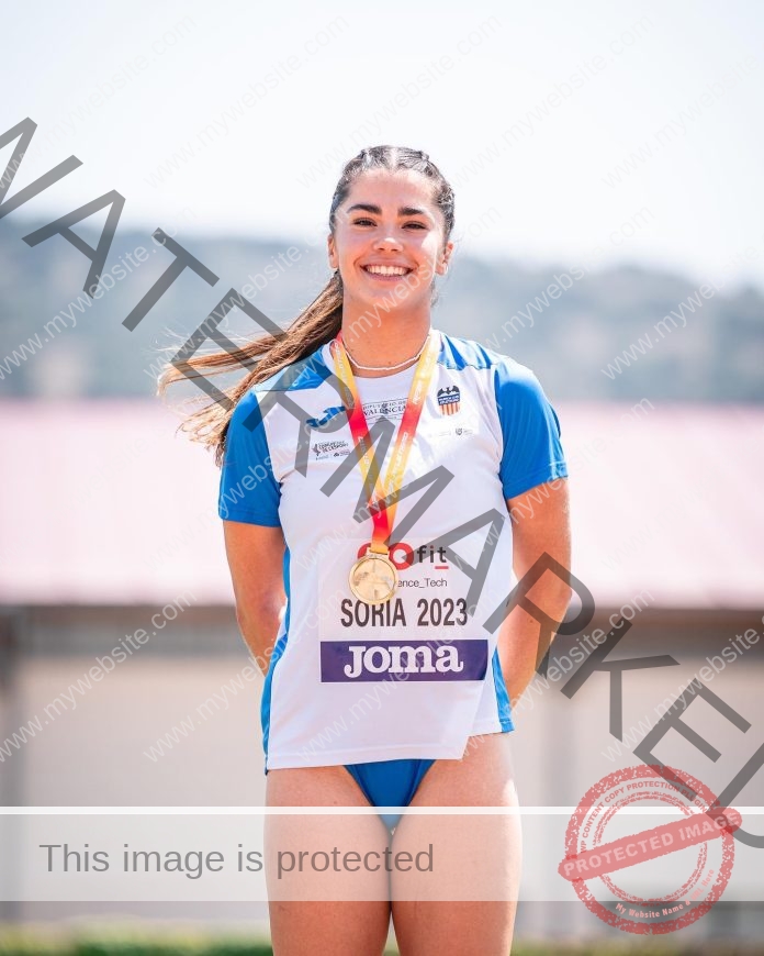 Sofia Cosculluela, a Spanish track athlete in blue and white, smiles with a gold medal. Her race bib reads SORIA 2023.