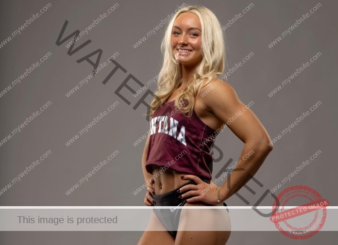 Tara Ohlwiler, a smiling woman with long blonde hair, poses confidently in maroon Montana track gear against a gray background.