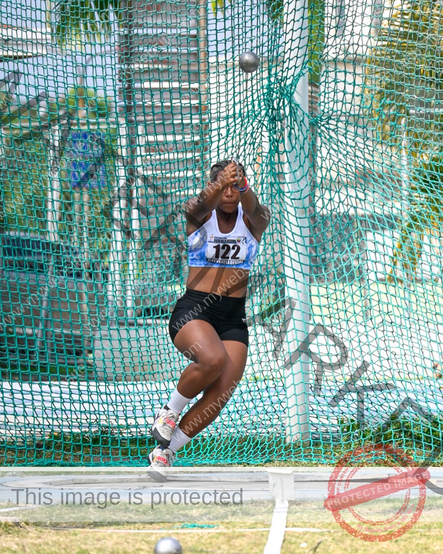 yenni-veroes-venezuela-yenni__throw-052 Alejandra Veroes An athlete wearing a numbered bib and sportswear is mid-spin in a hammer throw cage, gripping the hammer, ready to release.