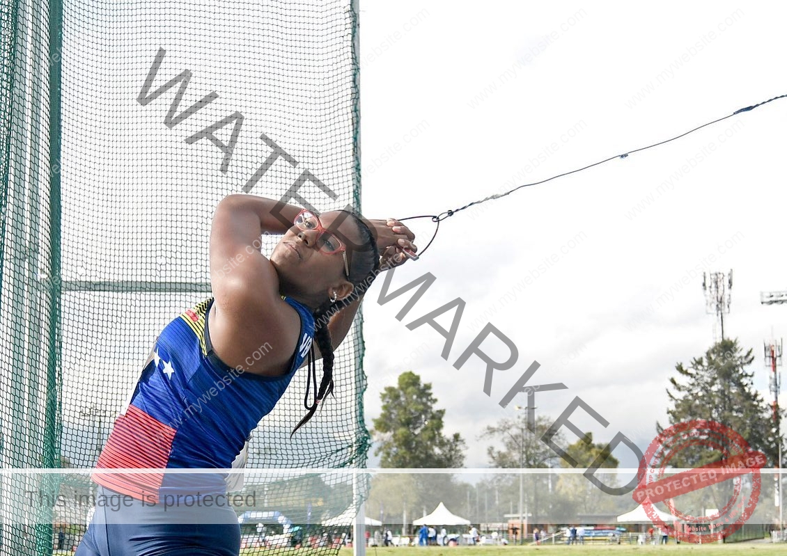 yenni-veroes-venezuela-yenni__throw-065 Alejandra Veroes, an athlete in a blue uniform, prepares to throw a hammer at an outdoor facility with trees and tents nearby.