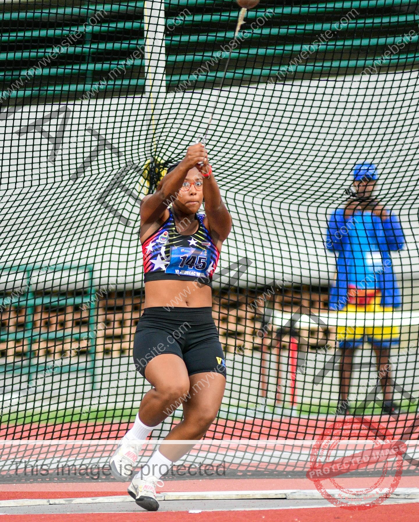 yenni-veroes-venezuela-yenni__throw-083 Alejandra Veroes A female athlete in sportswear spins and throws a hammer inside a netted cage, as someone in blue and yellow watches.