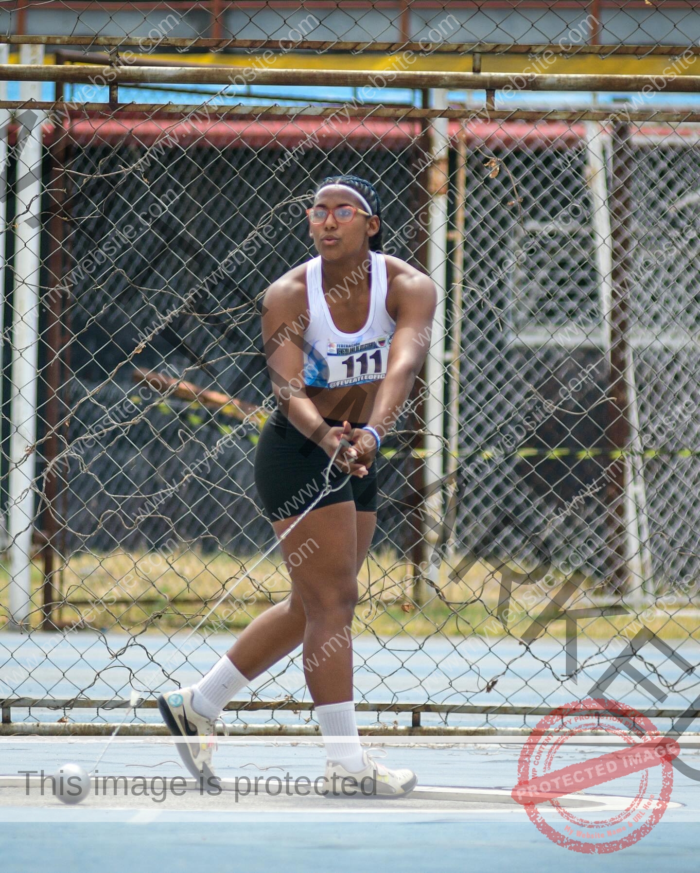 yenni-veroes-venezuela-yenni__throw-084 Alejandra Veroes A female athlete in sportswear prepares to throw a hammer during a track and field event, inside a fenced cage.