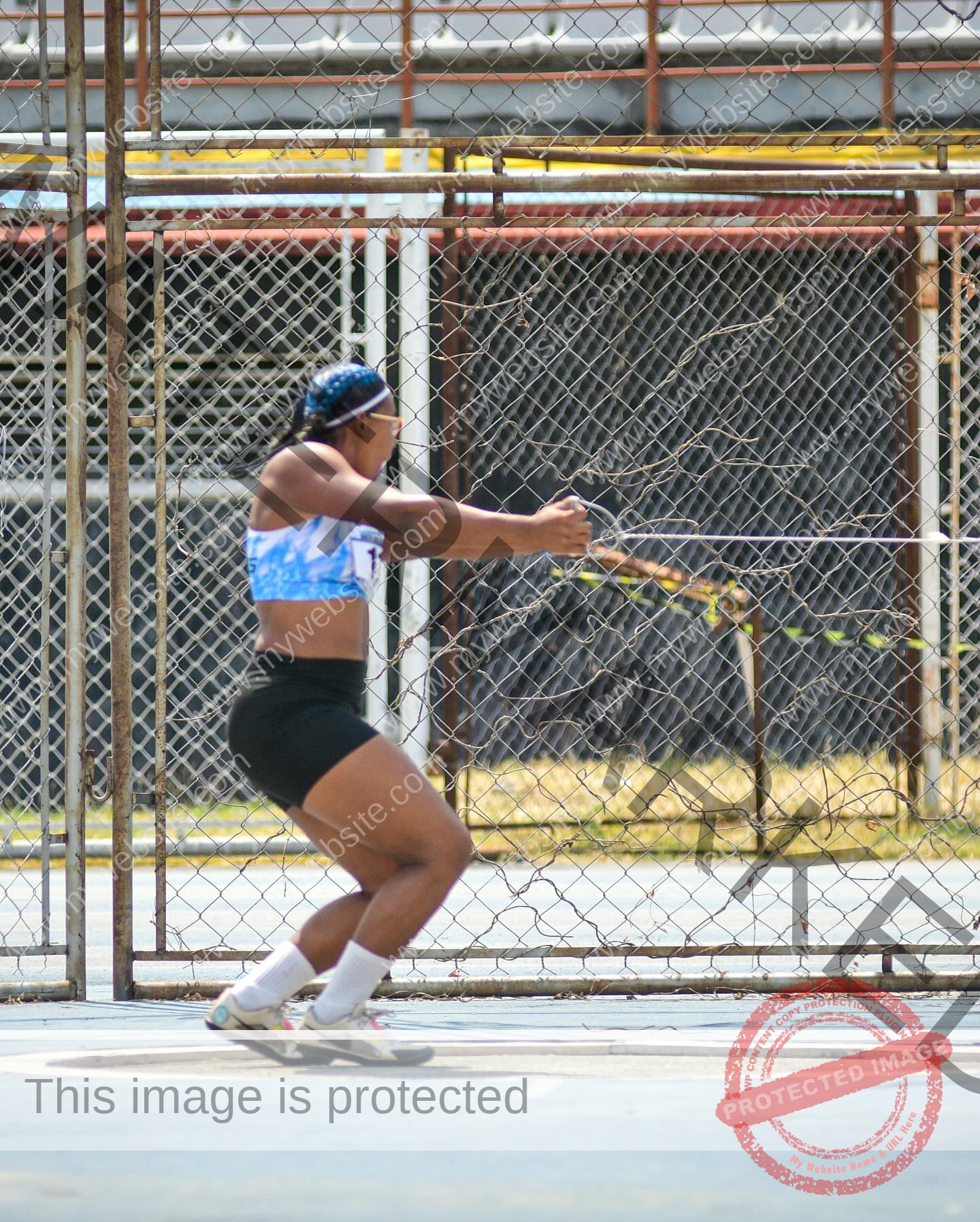 yenni-veroes-venezuela-yenni__throw-085 Yenni Veroes, wearing athletic gear, stands in a fenced sports area, focused and ready to throw a discus held with both hands.