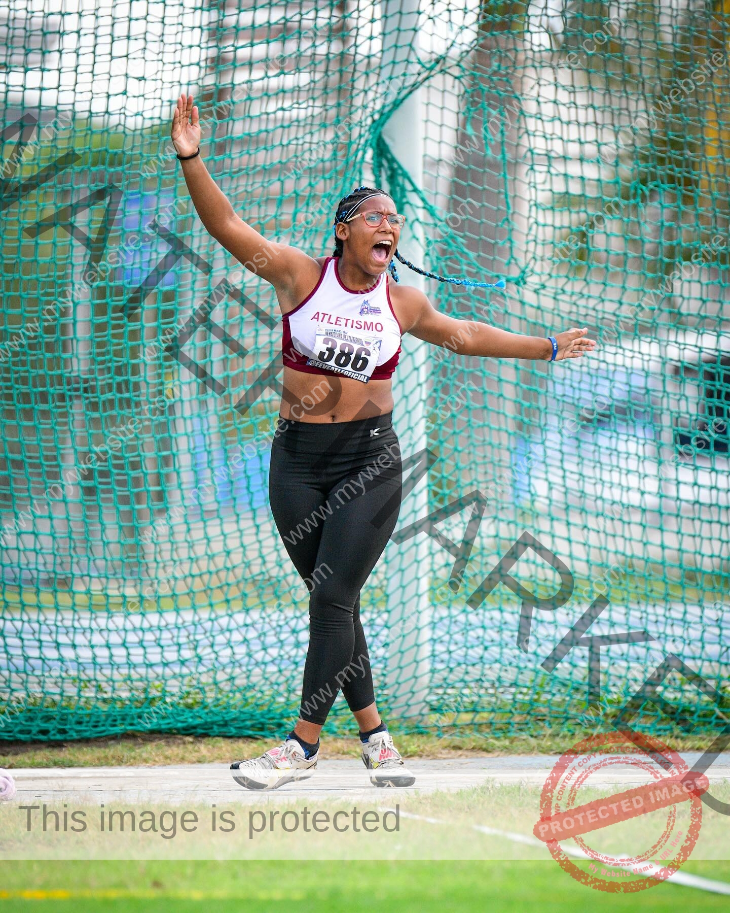 yenni-veroes-venezuela-yenni__throw-093 Yenni Veroes, a female athlete in a red and white top and black leggings, celebrates arms raised, smiling near a green net, bib 386.