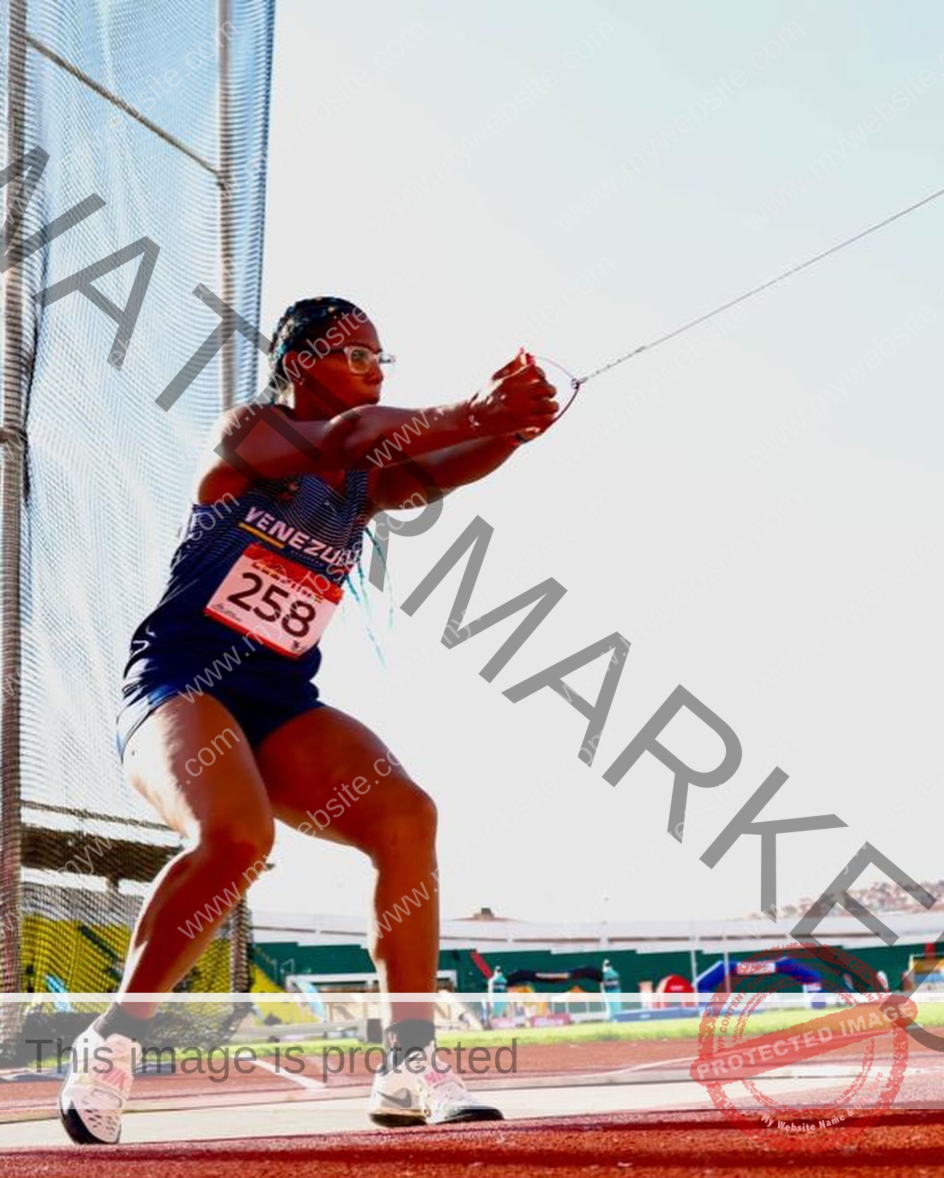 yenni-veroes-venezuela-yenni__throw-100 Alejandra Veroes A female athlete from Venezuela, in blue uniform with bib 258, prepares to spin for hammer throw in a sunny cage.