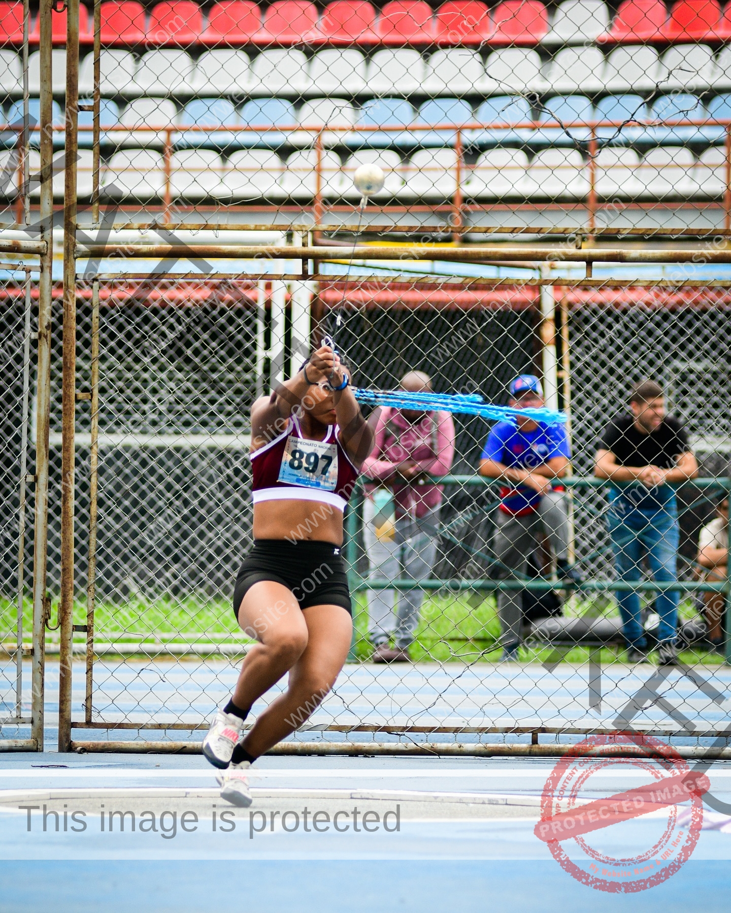 yenni-veroes-venezuela-yenni__throw-111 Yenni Veroes A female athlete in sportswear, number 897, swings a hammer in a fenced cage at a track and field event as onlookers watch.