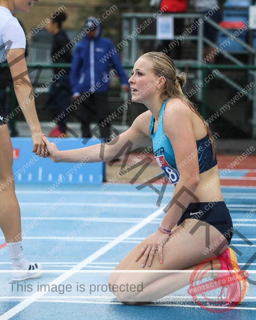amaya-kruse-jorgensen-denmark-amayajorgensen-0254 Amaya Kruse Jorgensen, track and field star from Denmark, kneels on a wet track, reaching to be helped up by another runner.