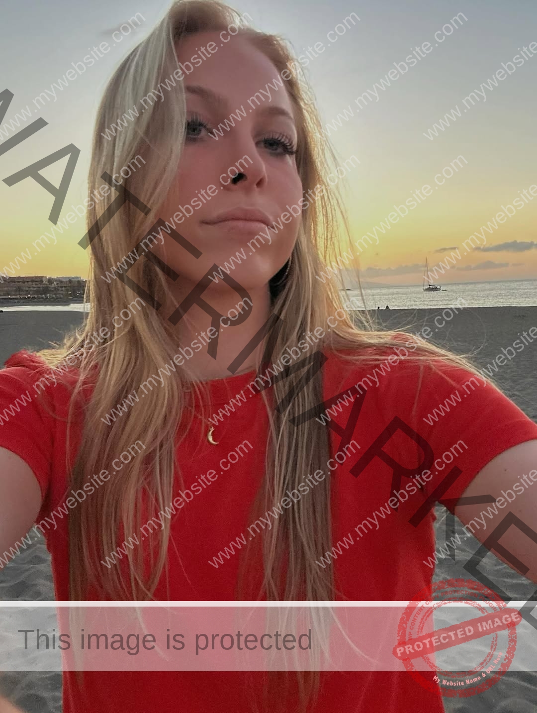 amaya-kruse-jorgensen-denmark-amayajorgensen-0300 Amaya Kruse Jorgensen, track and field star from Denmark, with long blonde hair in a red shirt takes a sunset beach selfie; sailboat behind.