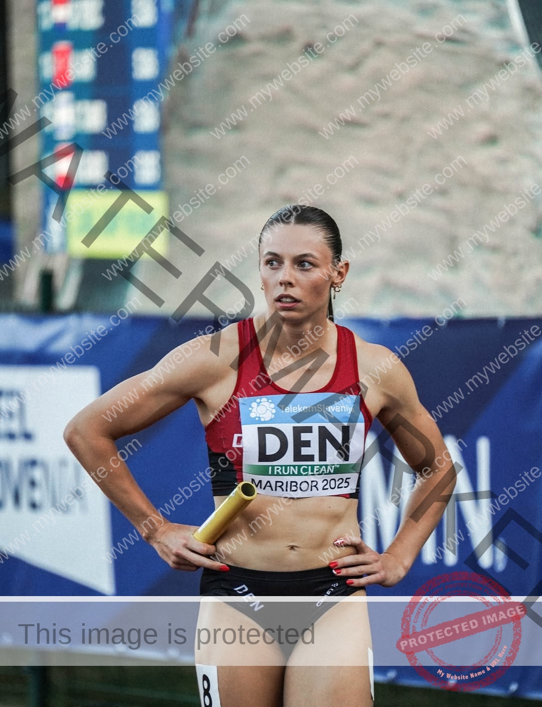 amaya-kruse-jorgensen-denmark-amayajorgensen-0308 Amaya Kruse Jorgensen, track and field star from Denmark, in a red/black DEN uniform holds a baton, glancing aside at competition.