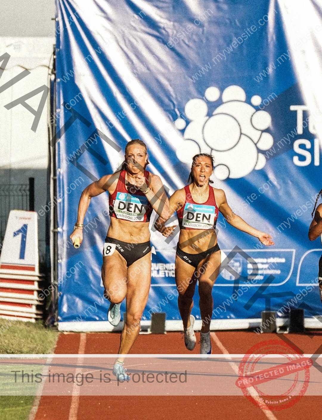 amaya-kruse-jorgensen-denmark-amayajorgensen-0311 Amaya Kruse Jorgensen, track and field star from Denmark, hands off a relay baton to a teammate on a track with blue event banner.