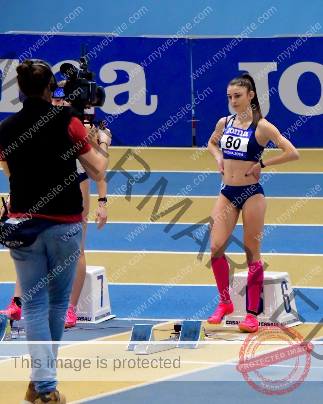 anabel-vitale-italy-anabelvitale-0522 Anabel Vitale, track and field star from Italy, stands in pink knee socks at the starting blocks as a camera films her on an indoor track.