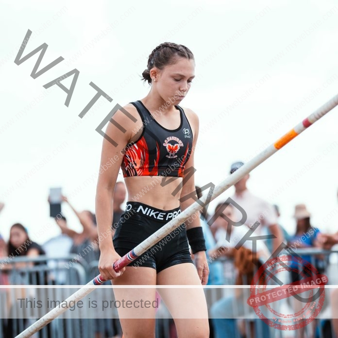 Camila Rodriguez, track and field star from Argentina, in athletic gear grips her pole and looks down as she prepares to pole vault.