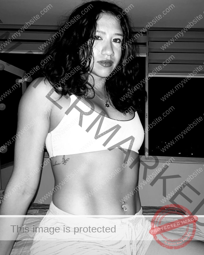 Camila Salinas, track and field star from Ecuador, poses confidently indoors at night in a white crop top and shorts; B&W photo.