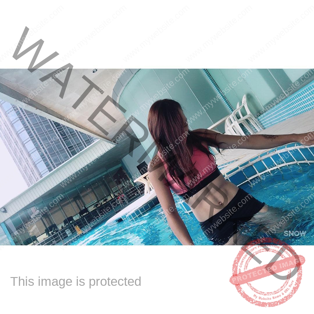 chan-pui-kei-hong-kong-chanpuikeii-02713 Chan Pui Kei, track and field star from Hong Kong, stands in a pool in pink sports top and black shorts, looking down by the edge.