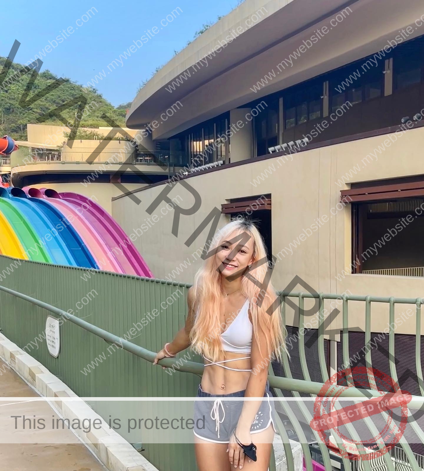 chan-pui-kei-hong-kong-chanpuikeii-02864 Chan Pui Kei, track and field star from Hong Kong, with long blonde hair, smiles in white bikini top by water slides at an outdoor park.