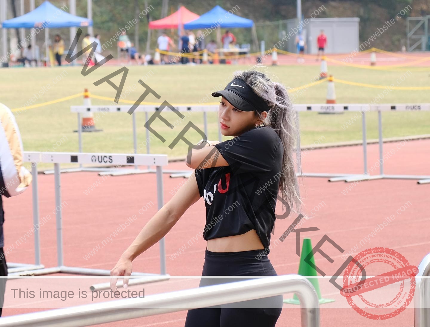 chan-pui-kei-hong-kong-chanpuikeii-02890 Chan Pui Kei, track and field star from Hong Kong, with silver hair stretches her arm on an outdoor track in black sportswear and visor.