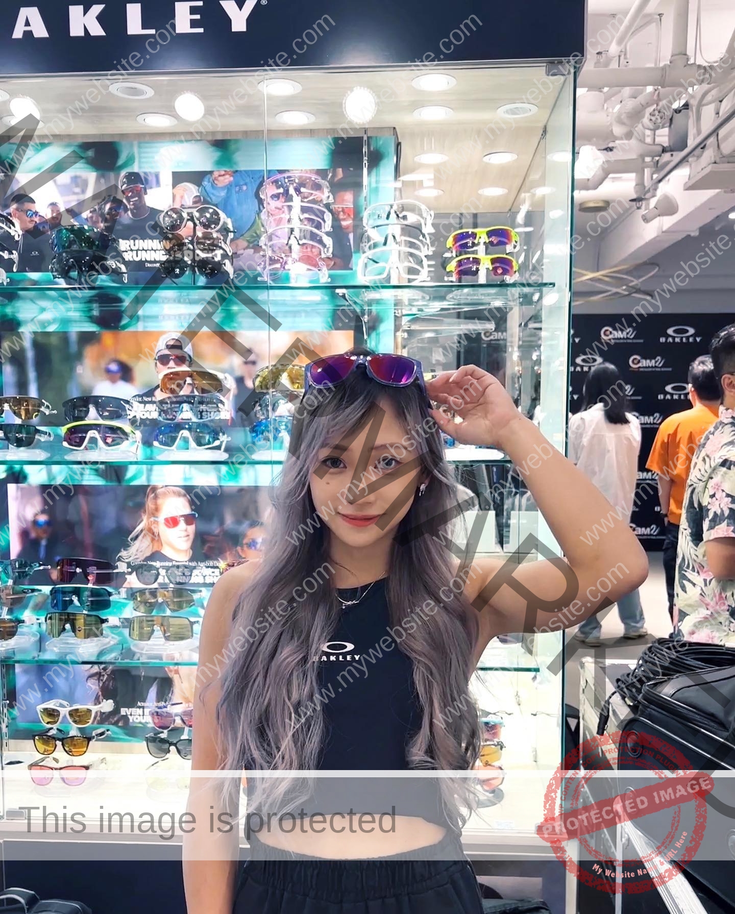 chan-pui-kei-hong-kong-chanpuikeii-02907 Chan Pui Kei, track and field star from Hong Kong, with long wavy gray hair, smiles holding sunglasses in an Oakley store.