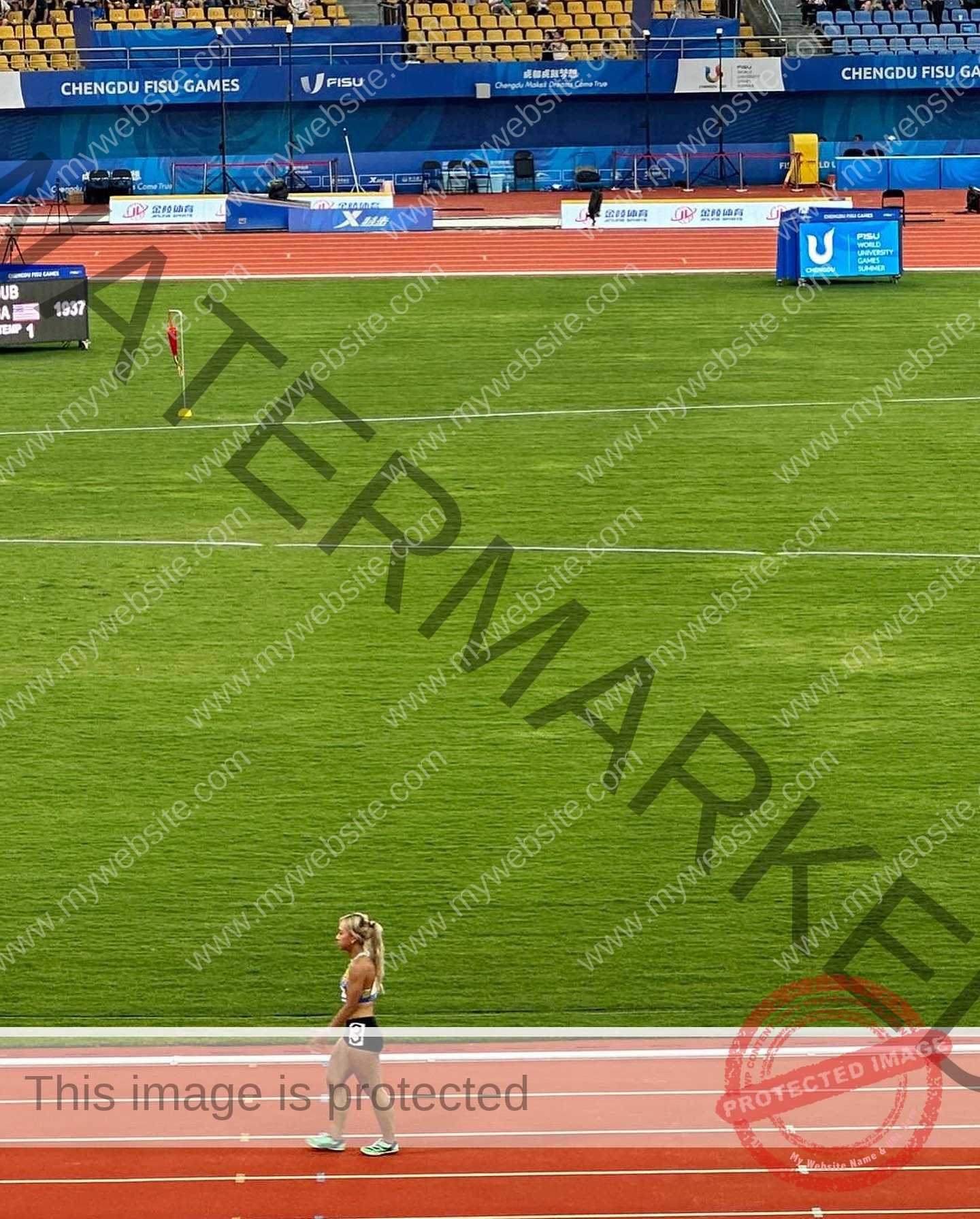 chan-pui-kei-hong-kong-chanpuikeii-02937 Chan Pui Kei, track and field star from Hong Kong walks alone on a red running track in a stadium with green grass and empty yellow seats.