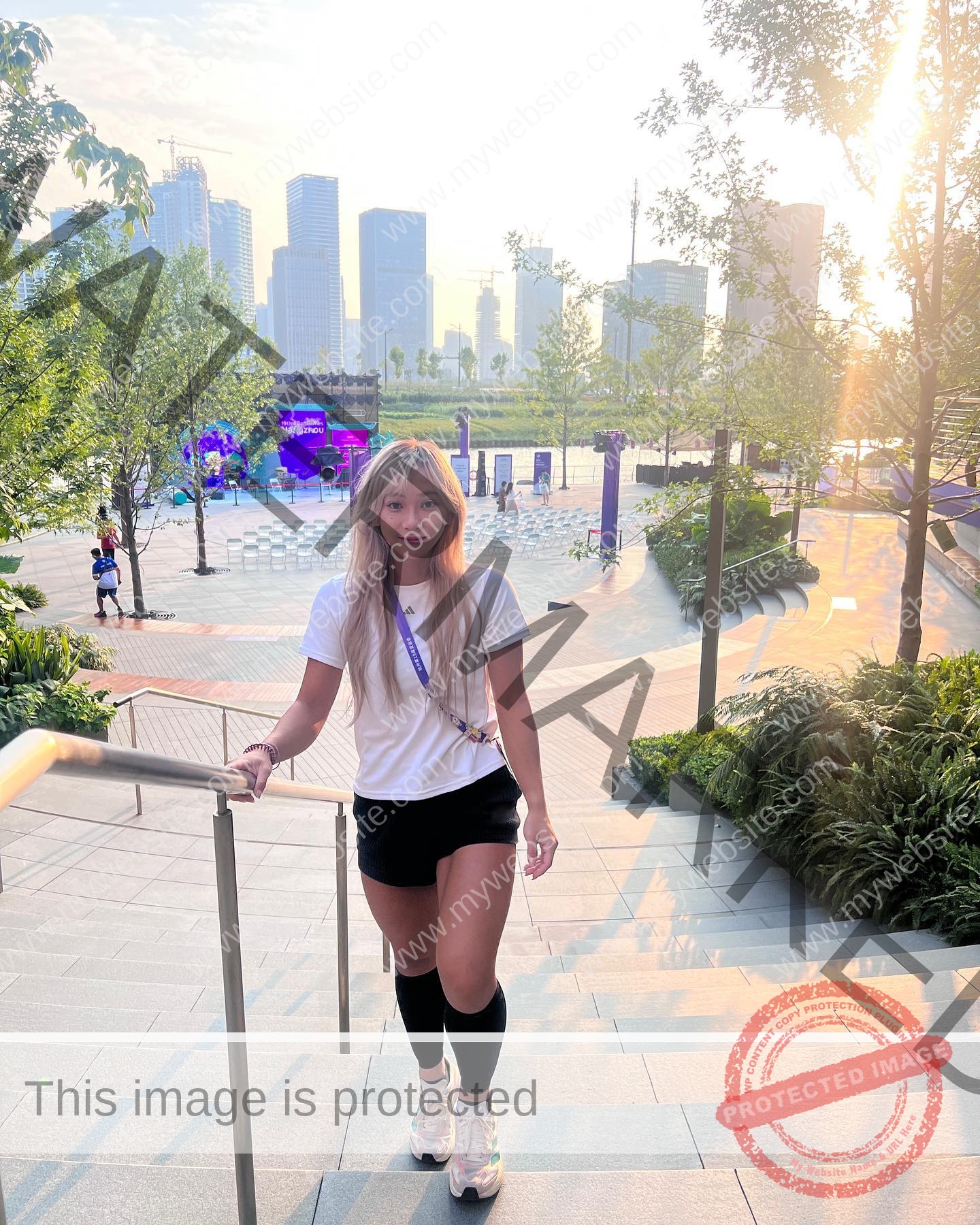 chan-pui-kei-hong-kong-chanpuikeii-02953 Chan Pui Kei, track and field star from Hong Kong, walks up outdoor steps in sportswear with a city skyline and event in the sunshine.