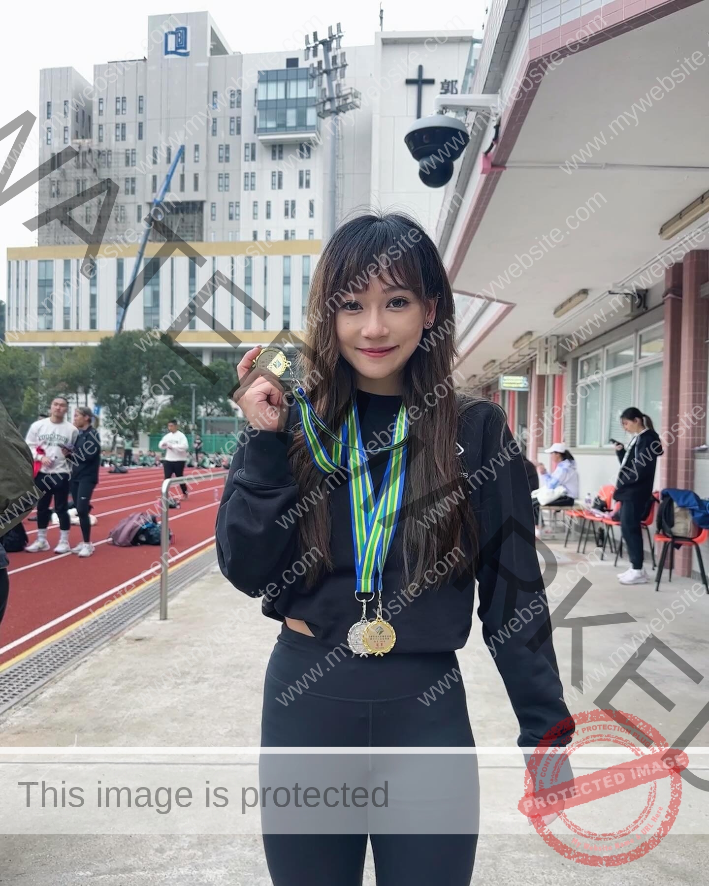 chan-pui-kei-hong-kong-chanpuikeii-02979 Chan Pui Kei, track and field star from Hong Kong, stands on a track smiling, holding a gold medal with two more medals around her neck.