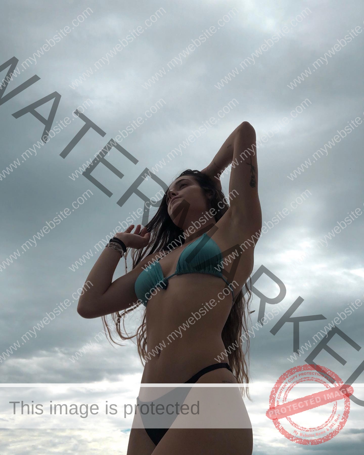 claudia-camacho-spain-clauudiacamacho-1385 Claudia Camacho, track and field star from Spain, poses outdoors in a teal bikini top and black bottoms against a cloudy sky.