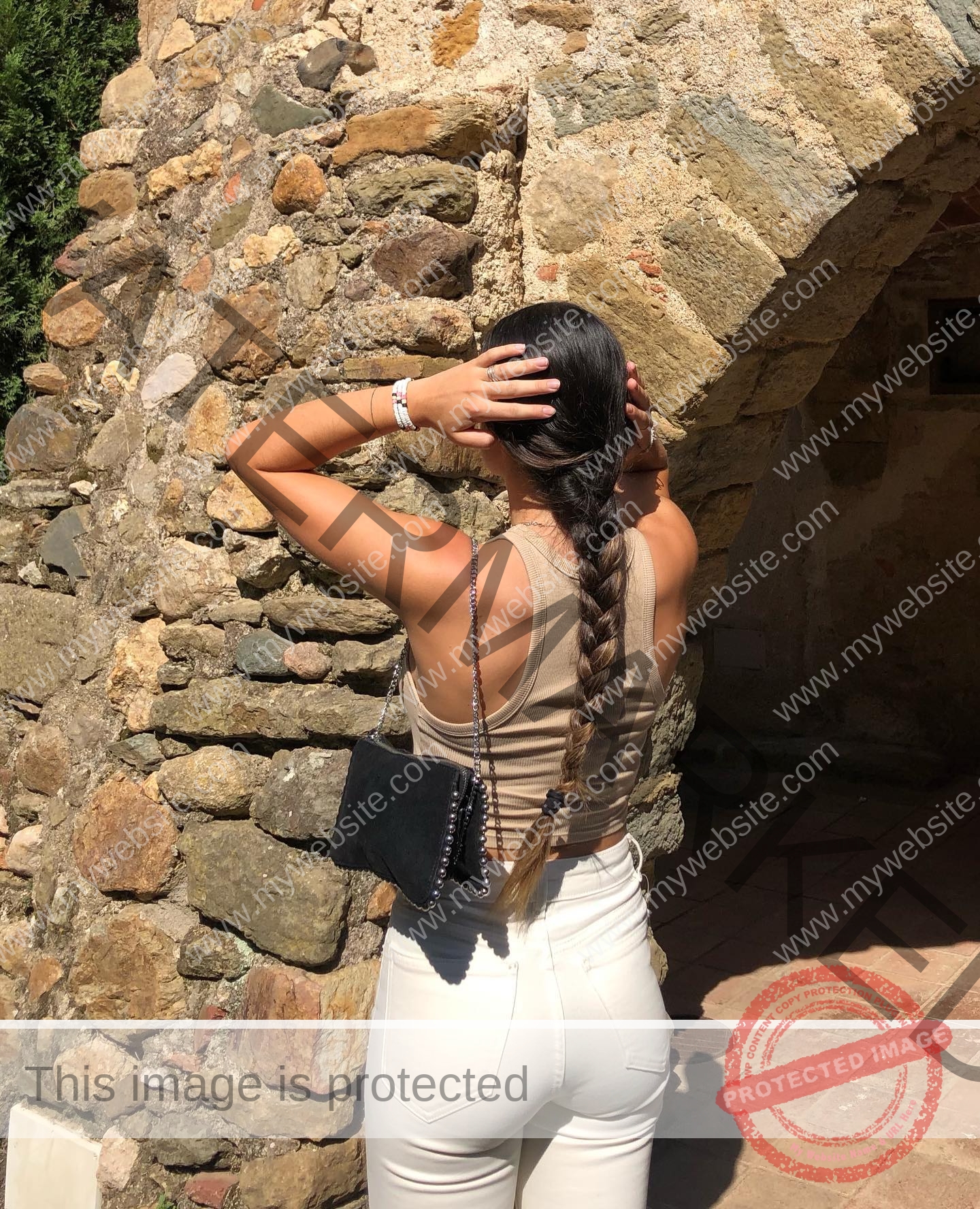 claudia-camacho-spain-clauudiacamacho-1391 Claudia Camacho, track and field star from Spain, with a long braid in beige tank top and white pants, stands by a rustic stone arch.