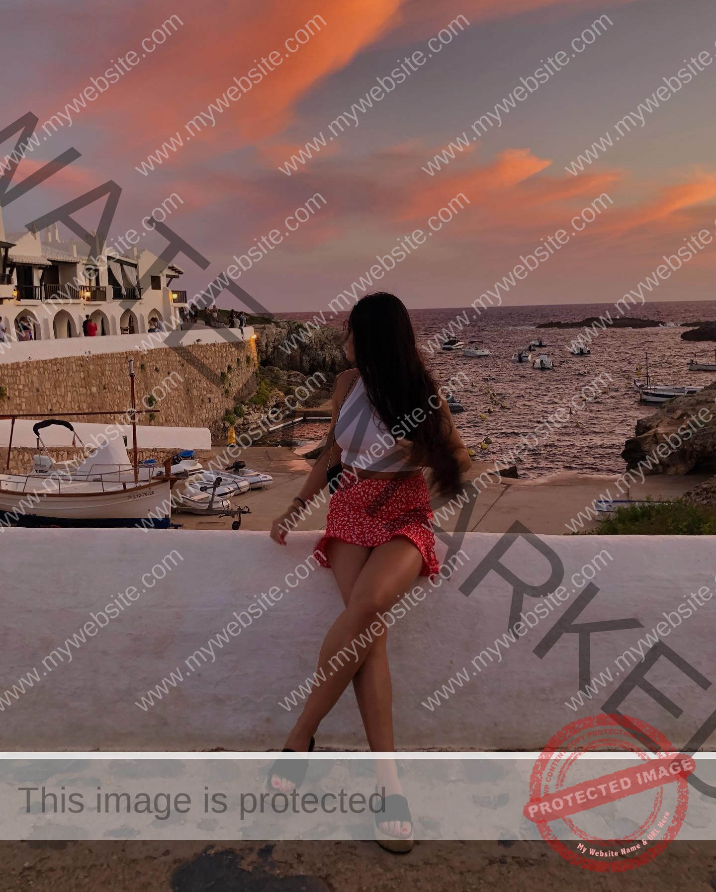 claudia-camacho-spain-clauudiacamacho-1402 Claudia Camacho, track and field star from Spain sits on a white wall in a white top and red skirt, gazing at boats at sunset.