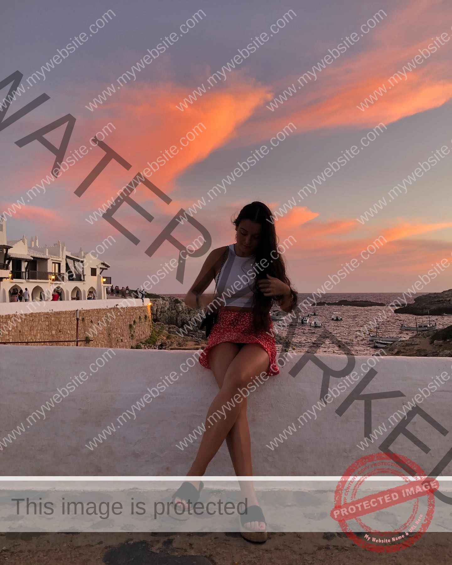 claudia-camacho-spain-clauudiacamacho-1403 Claudia Camacho, track and field star from Spain, sits on a white wall at sunset in a white top and red skirt, adjusting her hair.