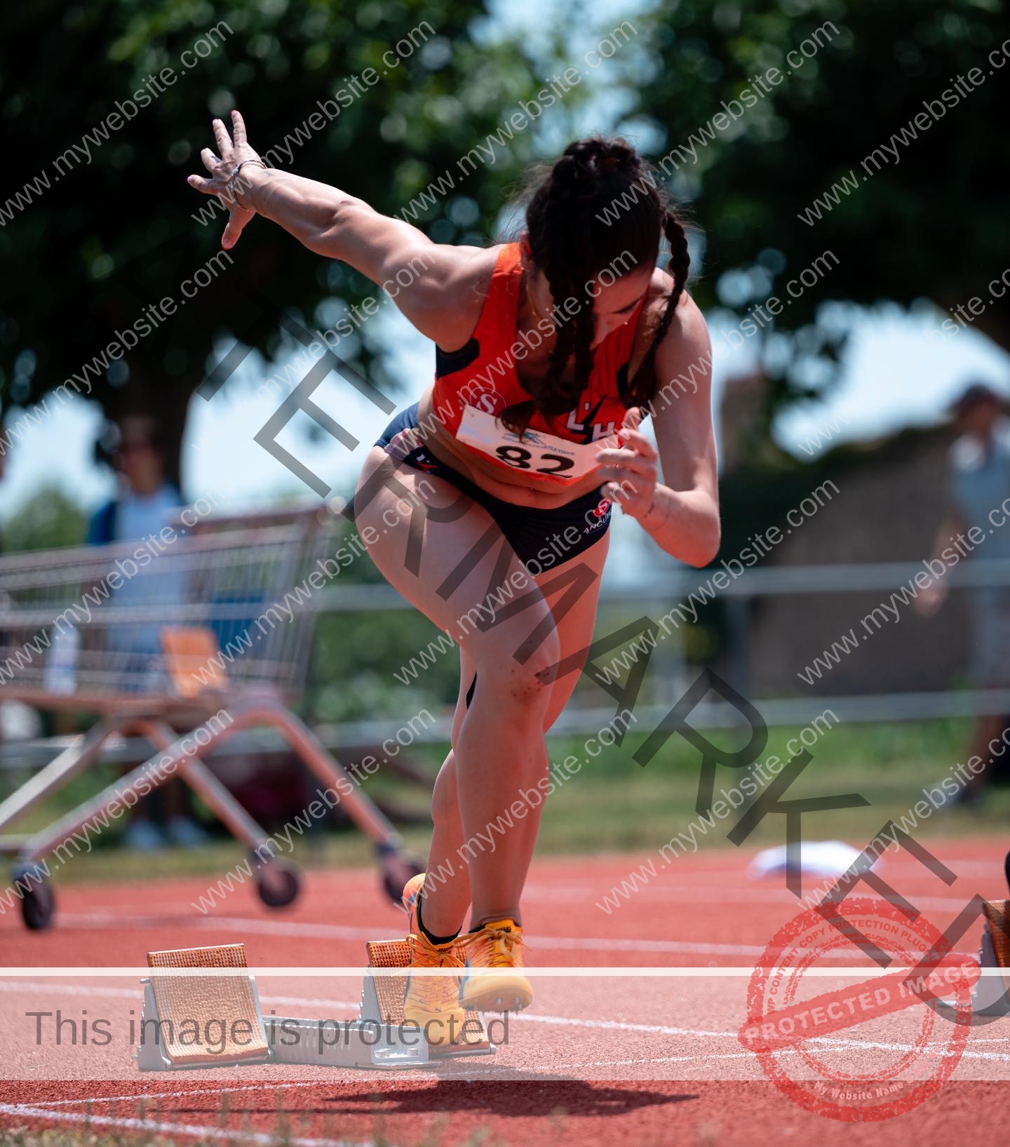 claudia-camacho-spain-clauudiacamacho-1407 Claudia Camacho, track and field star from Spain, sprints off starting blocks in orange top, black shorts; trees blur behind her.
