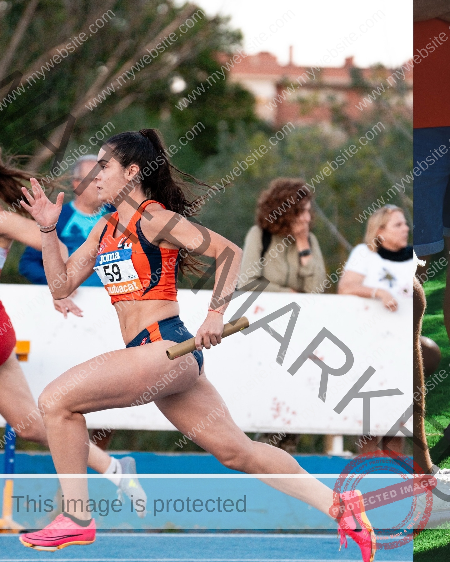claudia-camacho-spain-clauudiacamacho-1441 Claudia Camacho, track and field star from Spain, sprints in orange and blue with a baton as spectators watch behind a white barrier.