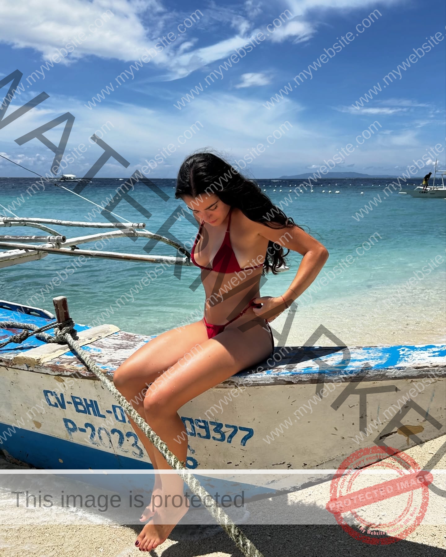 claudia-camacho-spain-clauudiacamacho-1453 Claudia Camacho, track and field star from Spain, sits in a red bikini on a boat by turquoise ocean under a clear blue sky.