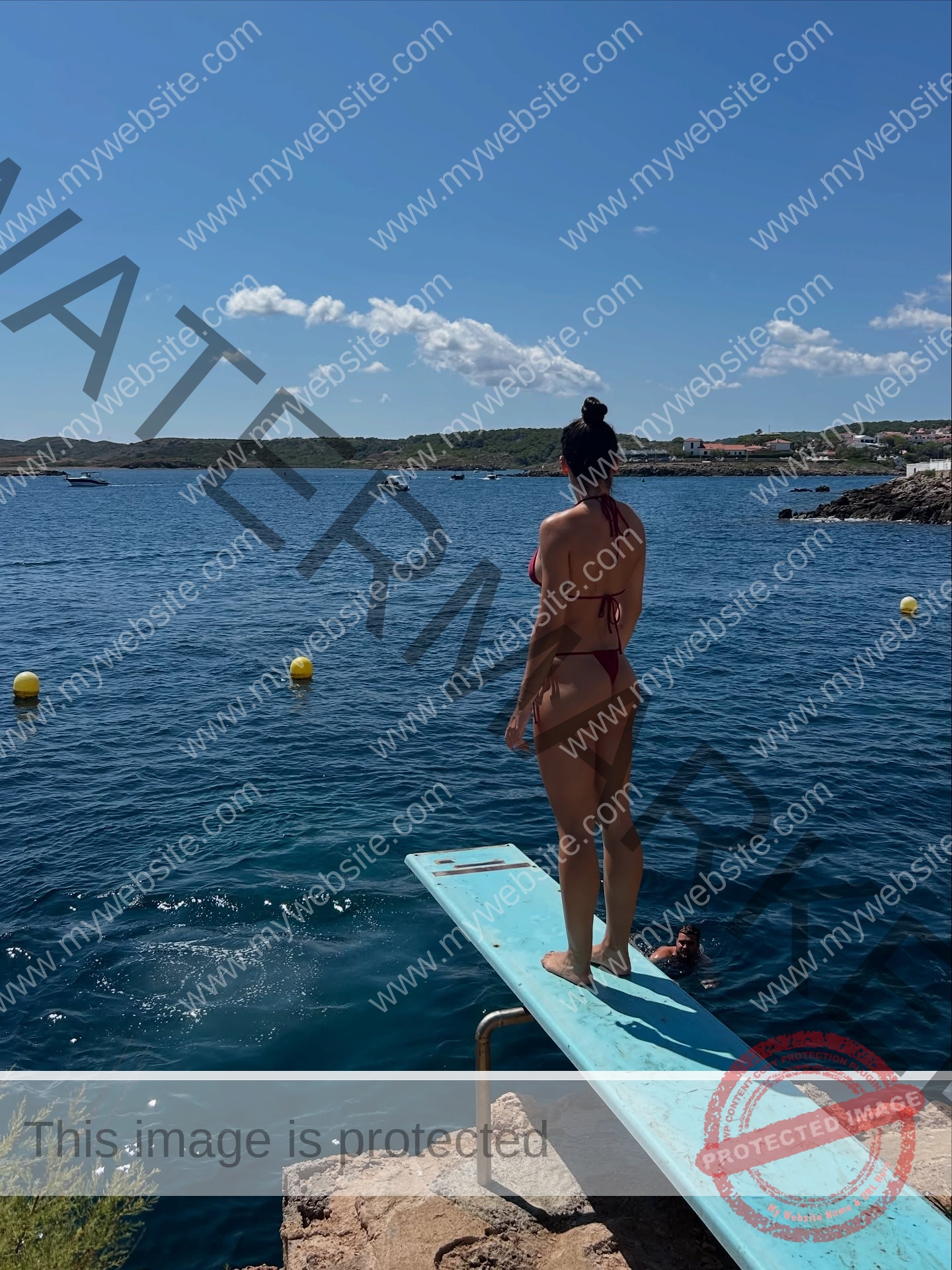 claudia-camacho-spain-clauudiacamacho-1469 Claudia Camacho, track and field star from Spain, stands in a pink bikini on a diving board above a calm blue sea with yellow buoys.