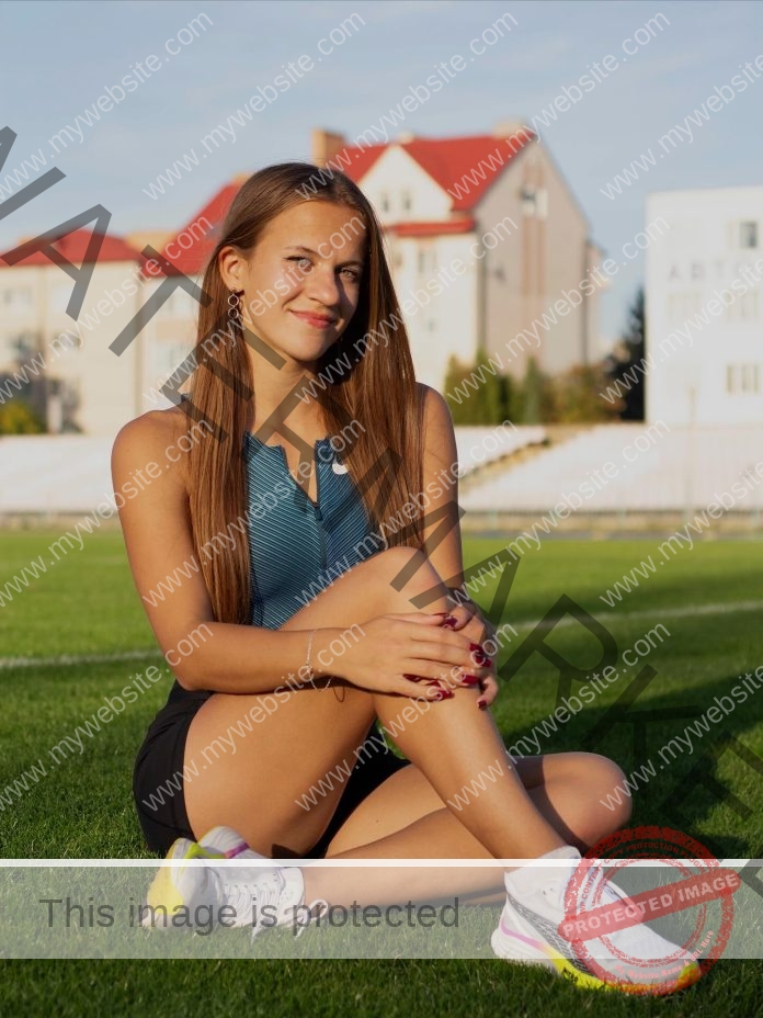 Diana Prymachuck, track and field star from Ukraine, sits cross-legged on grass, smiling in blue top and black shorts.