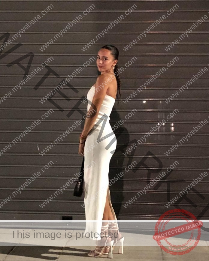 Eleni Vidouri, track and field star from Greece, stands sideways in a white strapless dress and heels, holding a black purse.