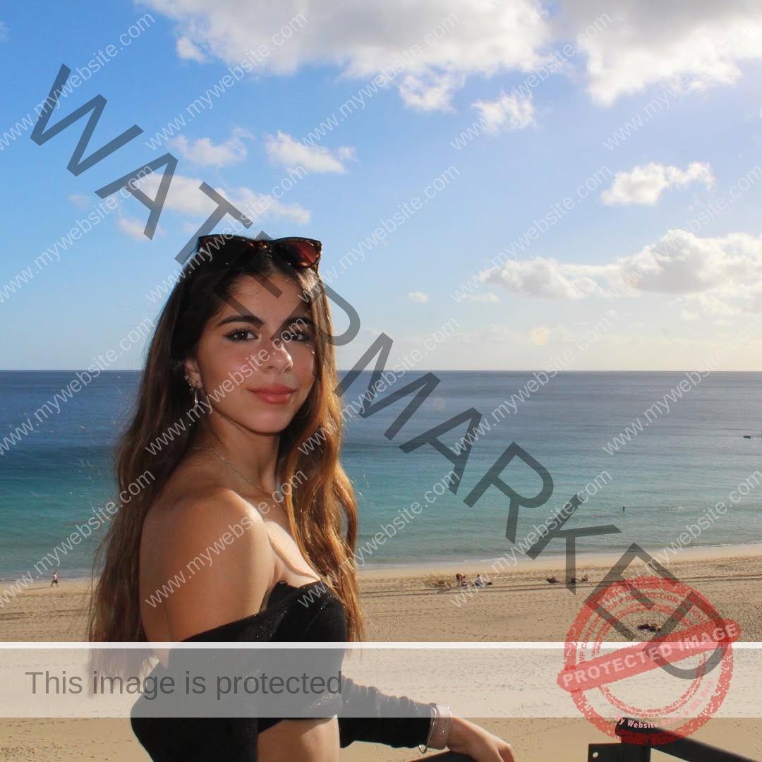 emma-deana-spain-emmadeana-15396 Emma Deana, track and field star from Spain, stands on a beachside terrace in a black off-shoulder top, ocean behind her.