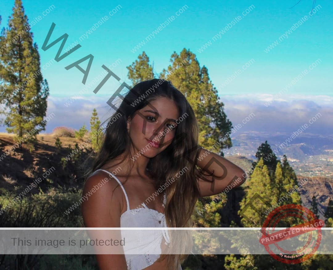 emma-deana-spain-emmadeana-15400 Emma Deana, track and field star from Spain, with long brown hair in a white top, poses outdoors among trees and mountain views.