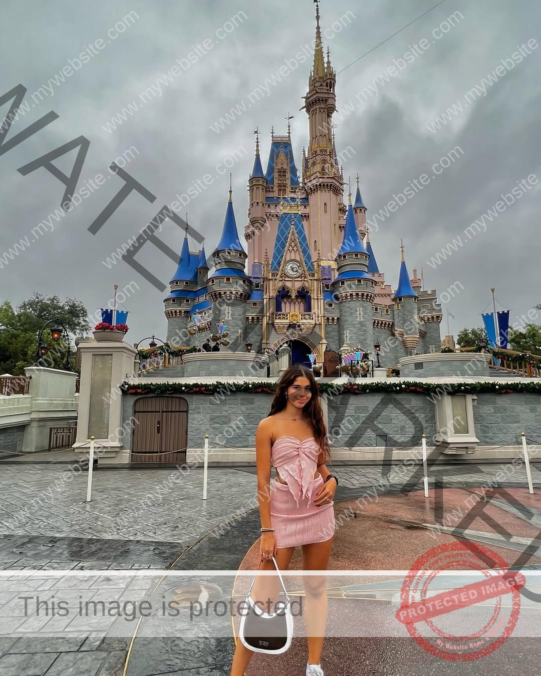 emma-deana-spain-emmadeana-15427 Emma Deana, track and field star from Spain, in a pink dress smiles by Cinderella Castle at Disney World, holding a white-brown bag.