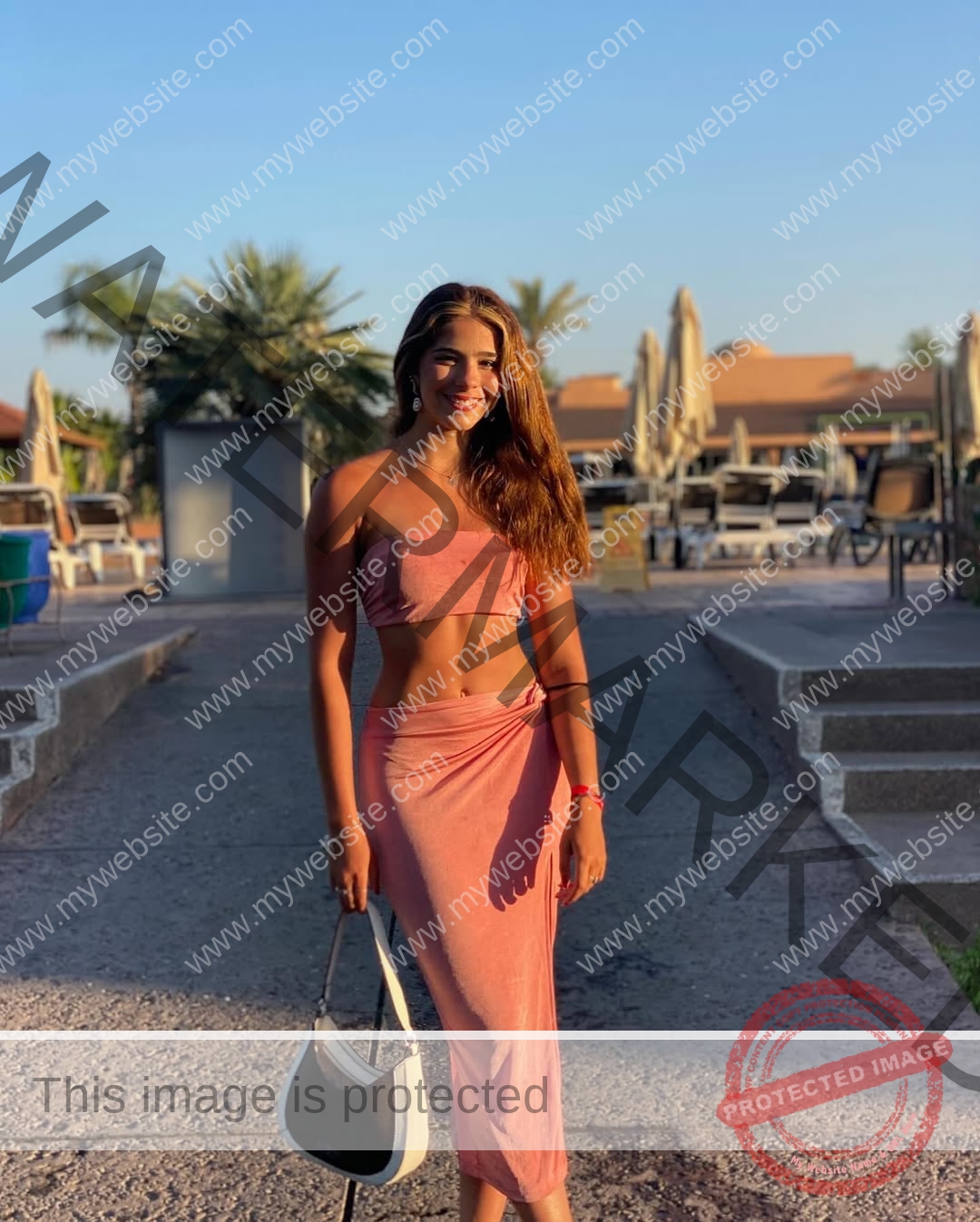 emma-deana-spain-emmadeana-15429 Emma Deana, track and field star from Spain stands outdoors in a pink two-piece, smiling and holding a black and white handbag.